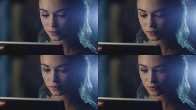 一个漂亮的年轻女孩在黑暗中拿着工作平板电脑的肖像照片。