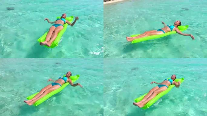 特写: 微笑的比基尼年轻女子在漂浮在热带岛屿清澈的海洋水面上的充气充气床垫上享受和放松