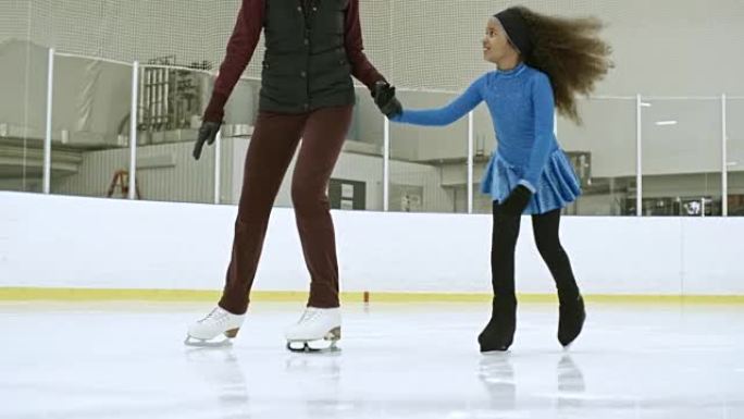 穿着裙子的小女孩和教练一起在冰上滑冰