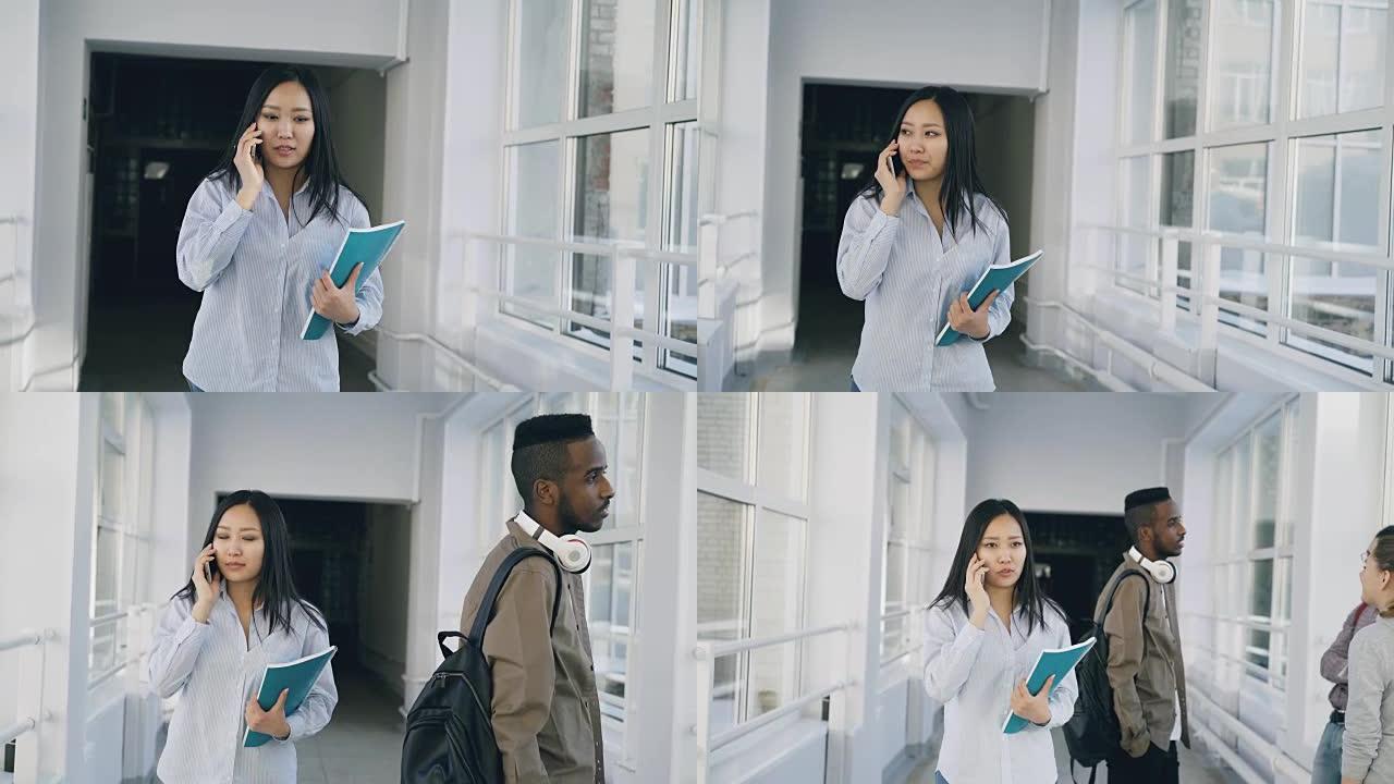 多莉 (Dolly) 拍摄的亚洲女学生在宽阔的大学走廊上行走，通过电话与其他多种族学生交谈