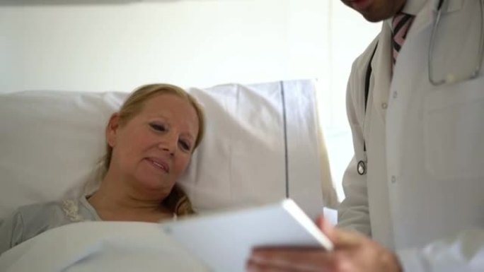 友好的医生叫醒他的高级病人，在数字平板电脑上向她展示血液检查结果