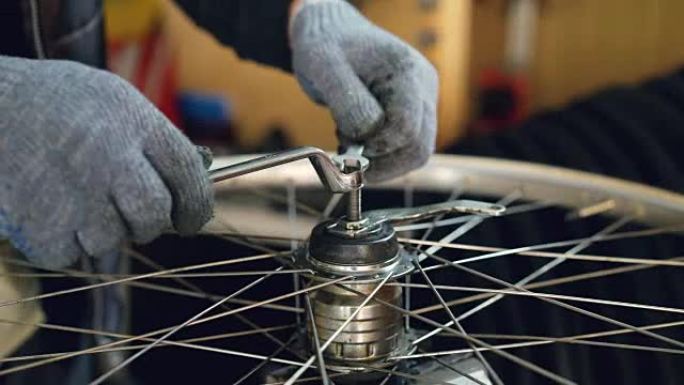 使用专业仪器扳手在自行车车轮机构中油腻手套拧紧螺钉的男性手的特写镜头。工作、人和职业概念。
