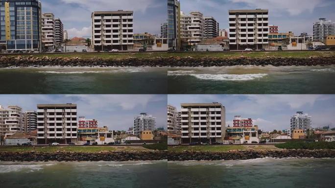 无人机沿着斯里兰卡科伦坡的海洋海岸街飞行。交通车辆和建筑物的空中跟踪镜头