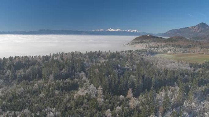 空中: 雾蒙蒙的冬天，高雪山和冰冷的冰冻森林后面的教堂