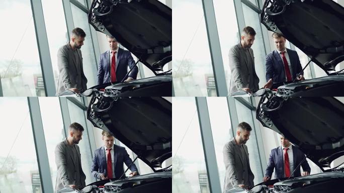 专业的汽车销售员正在演示汽车发动机罩下的客户汽车发动机，男人正在看着汽车零件并在谈论。买卖车辆概念。