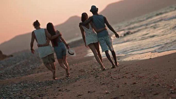 日落时浪漫的多民族时髦情侣在海滩上散步