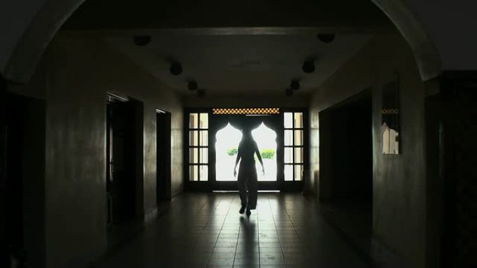 女人（剪影）穿过黑暗的阿拉伯大厅，走向阳光明媚的外部