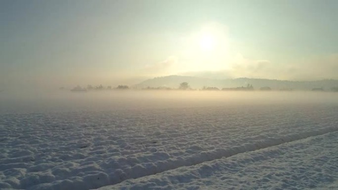 空中飞越被雪覆盖的雾蒙蒙的乡村，朝着郊区的小镇飞行