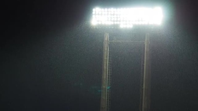 闪电体育场灯光的镜头在足球比赛之间的大雨中站立，下雨的天气有球迷欢呼的声音