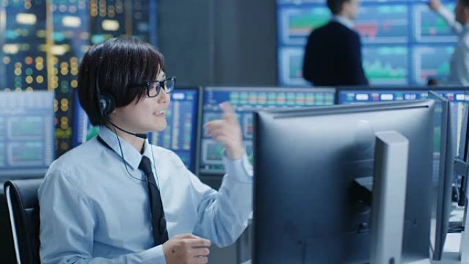 在网络运营中心，交易员用耳机拨打个人客户电话。在后台，交易者讨论监视器上显示的数据。