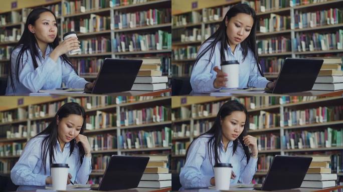 年轻的亚洲学生女孩坐在桌子旁，在大学图书馆里堆着书，用笔记本电脑工作，喝咖啡微笑着看着远处，准备考试