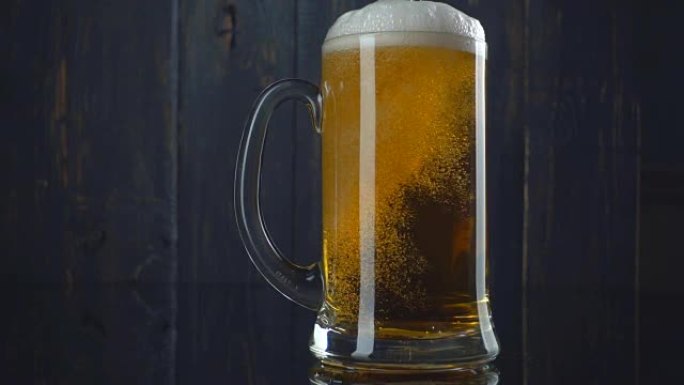将啤酒倒入深色木制背景上的玻璃中。慢动作