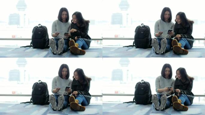 两名亚洲妇女在出发机场候机楼使用智能手机等待航班