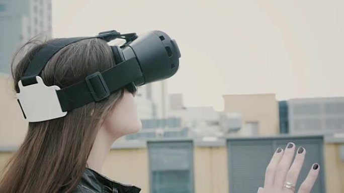 挥舞着头发的黑发女女孩在屋顶上使用虚拟现实眼镜。4k