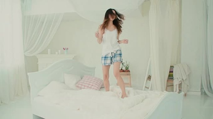 穿着睡衣的快乐年轻女子在床上跳跃。黑发女孩早上感到快乐。慢动作