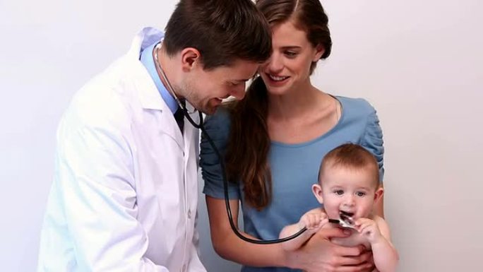 漂亮的母亲抱着婴儿，而儿科医生听他的胸部
