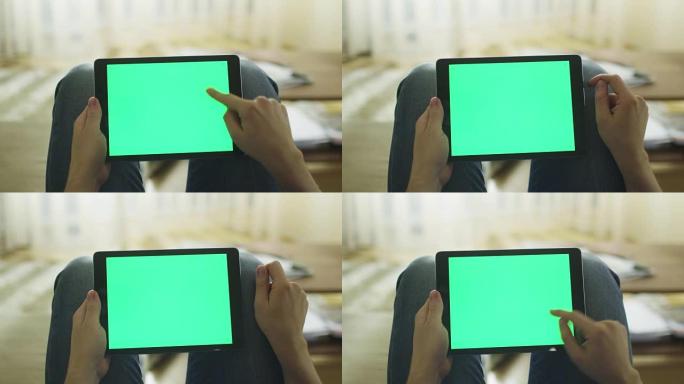 男子躺在家里的沙发上，并在膝盖上以横向模式使用带有绿色屏幕的平板电脑