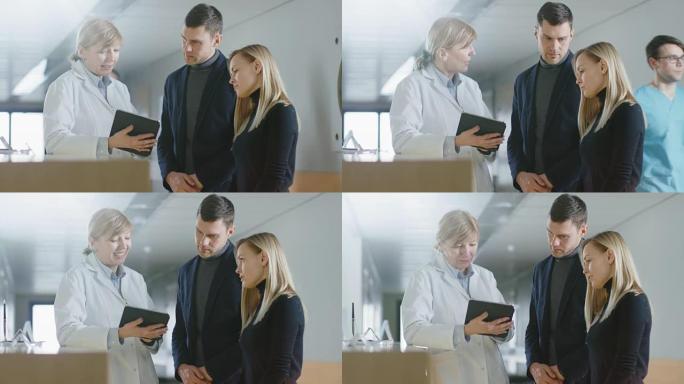 在医院的接待处，医生拿着平板电脑与这对年轻夫妇交谈。