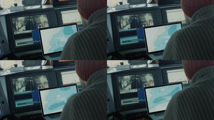 商业渔船的船长在他的船舱里被监视器和屏幕包围着，用海图工作。