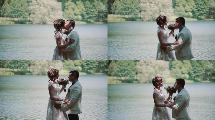 一对结婚那天接吻的夫妇的侧视图。快乐的新娘和新郎在河岸美丽的地方大笑