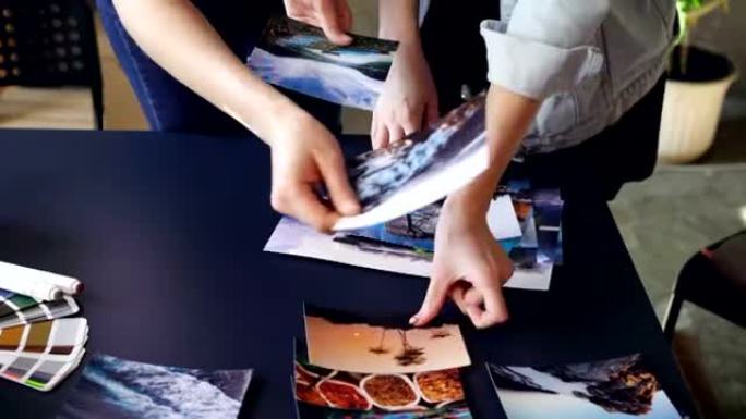 妇女的手的特写镜头将照片放在现代桌子上，并将它们分组。调色板、记号笔和茶杯在桌子上。