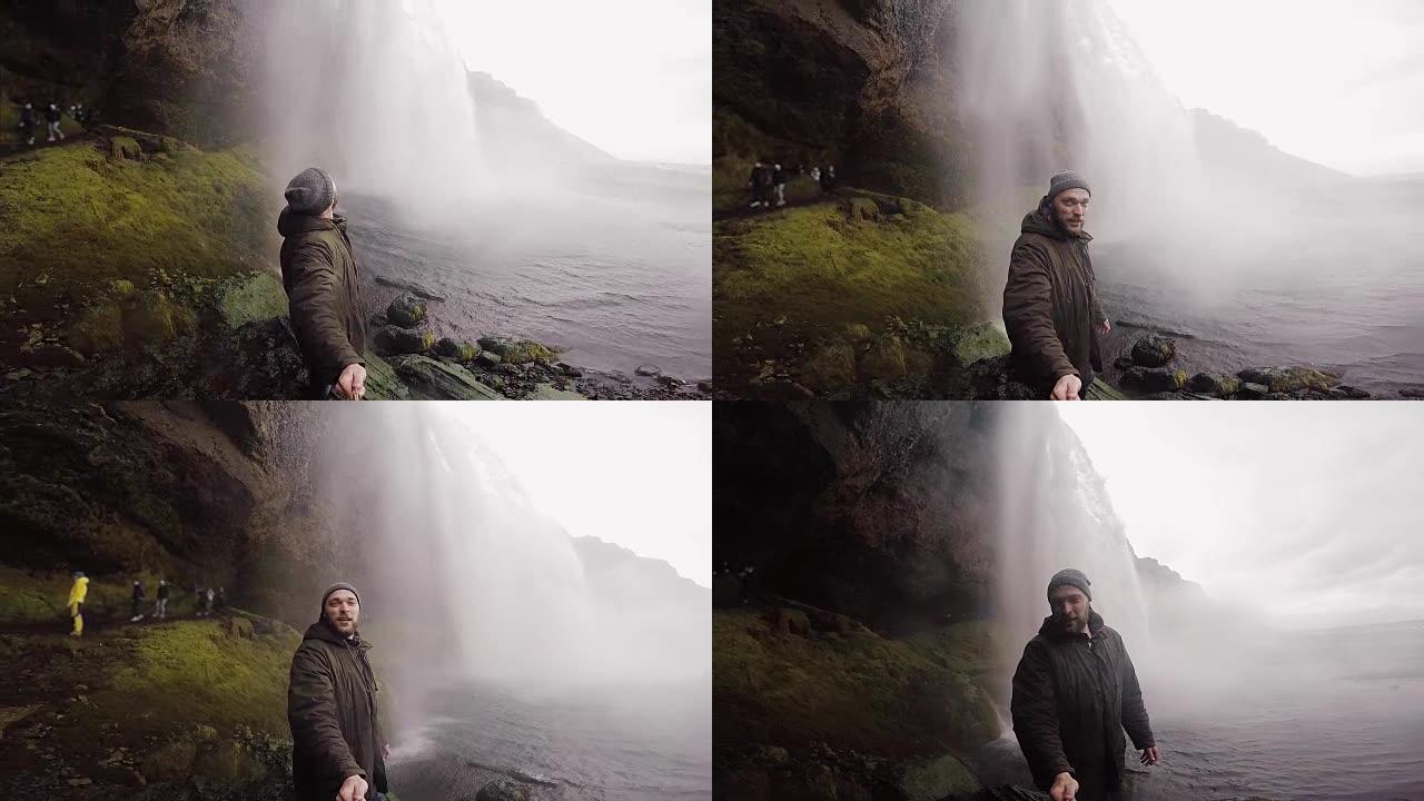 阴天，年轻的游客用自拍杆在gopro相机上拍摄冰岛强大的瀑布Seljalandsfoss