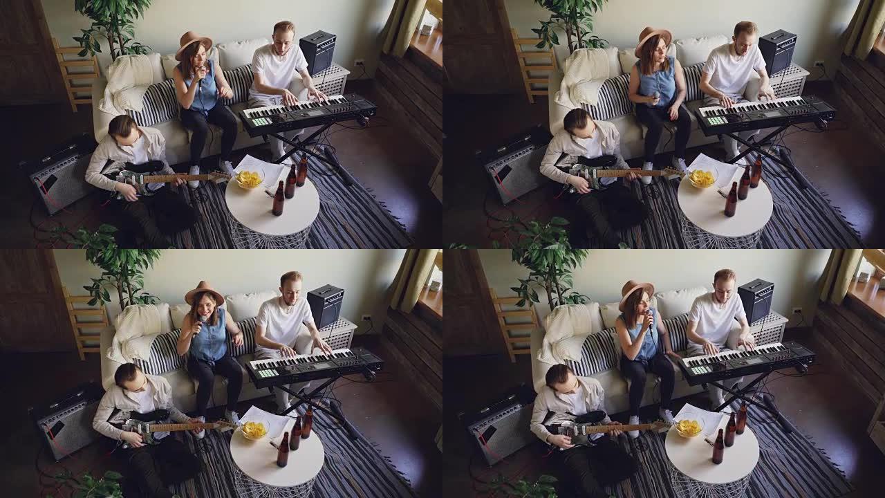 音乐乐队在家庭工作室排练的高角度视图。情绪活跃的年轻人正在弹奏乐器键盘，吉他和唱歌。