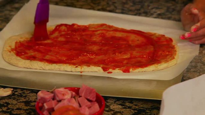 年轻女孩在披萨面团上涂番茄酱