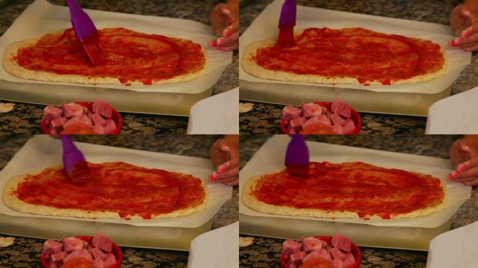 年轻女孩在披萨面团上涂番茄酱