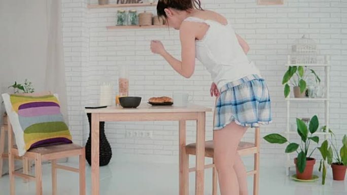 美丽的年轻女子在厨房早上跳舞。穿着睡衣的黑发女孩在家吃早餐