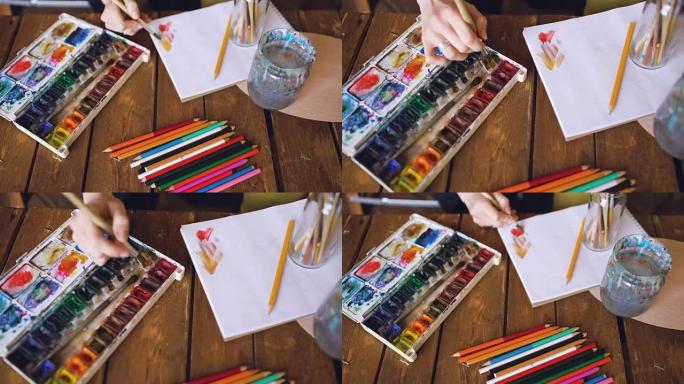 年轻女性艺术家用水彩颜料和画笔混合颜色特写绘制图片