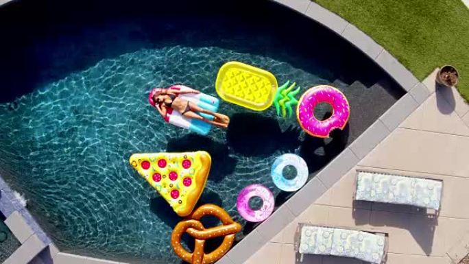 年轻女子躺在现代房子蓝色游泳池的有趣游泳池玩具上