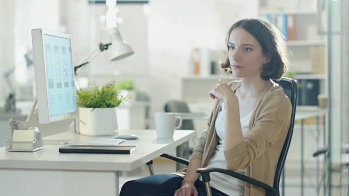 专注于创意的女人坐在办公室的台式电脑旁。想着解决问题，在她的椅子上打转。