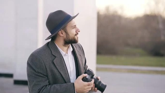 时尚的年轻摄影师戴着帽子站在户外，在旅行中拍摄游客观光