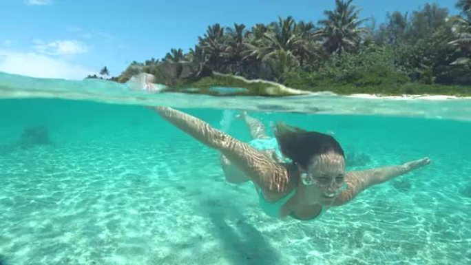在一个完美的夏日，关闭快乐的年轻女子在绿松石水中潜水