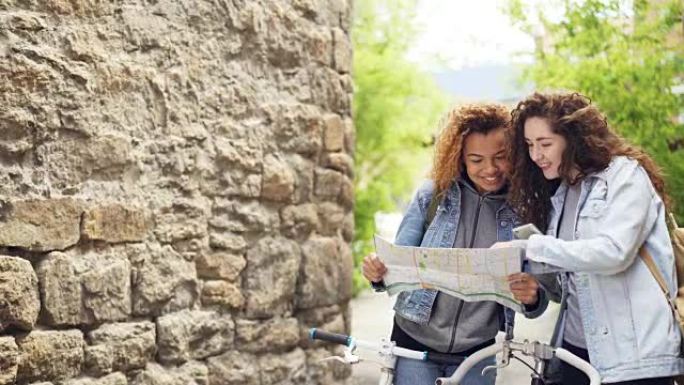 快乐的女人高兴的游客正在检查纸质地图和智能手机，在国外寻找正确的道路，有说有笑。现代技术和旅行理念。