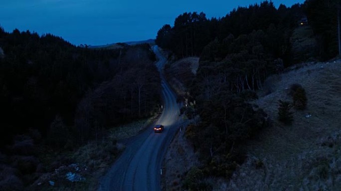 鸟瞰车在乡间小路上行驶，越野车在黄昏时驾驶，大灯穿过松树