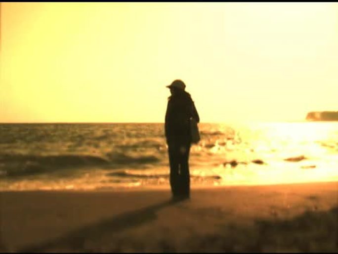 自由独立的女人在黄色的日落中站在海边