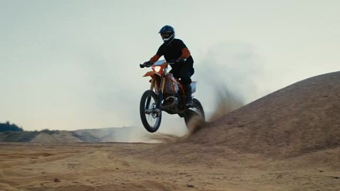 职业摩托车越野赛车手驾驶他的FMX摩托车在沙地越野赛道上越过沙丘。