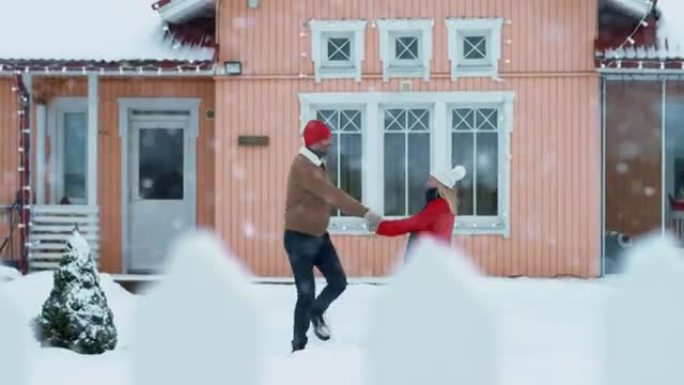 年轻美丽的夫妇跑出家门，走进覆盖着新鲜积雪的院子，他们旋转着跳舞。快乐的年轻人在神奇的冬天。