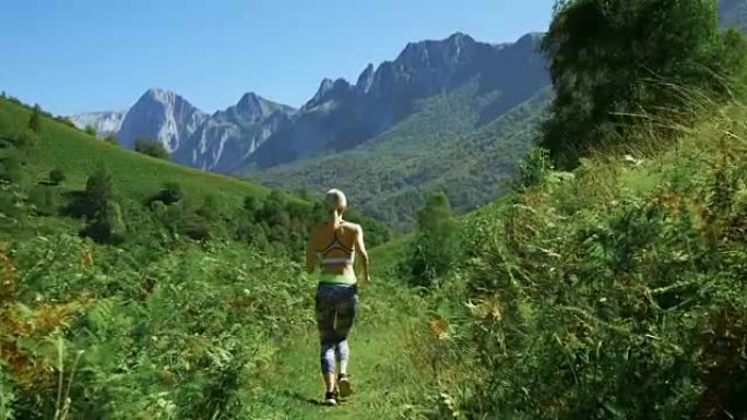 在美丽的健身女跑步者穿着运动服在小径上慢跑的镜头后，山景令人叹为观止。迷人的金发女孩和风景秀丽的大自
