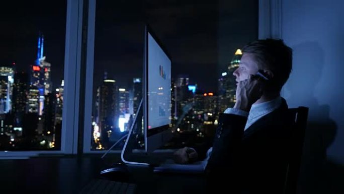 年轻成功的商人在现代办公室工作，晚上在电脑上分析图表。商务电话交谈。