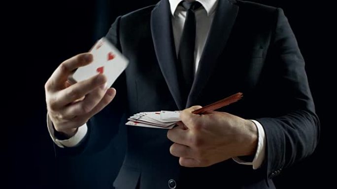 专业魔术师在一个黑色的西装表演卡戏法显示他的技能，使扇子出牌。背景是黑色的。