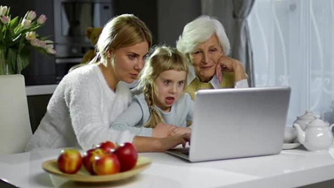可爱的妈妈和奶奶用笔记本电脑和女孩在一起