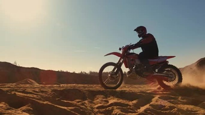 侧面镜头的专业摩托车越野赛摩托车骑手驾驶在沙丘和更远的越野轨道。这是《日落》，赛道上布满了烟雾。