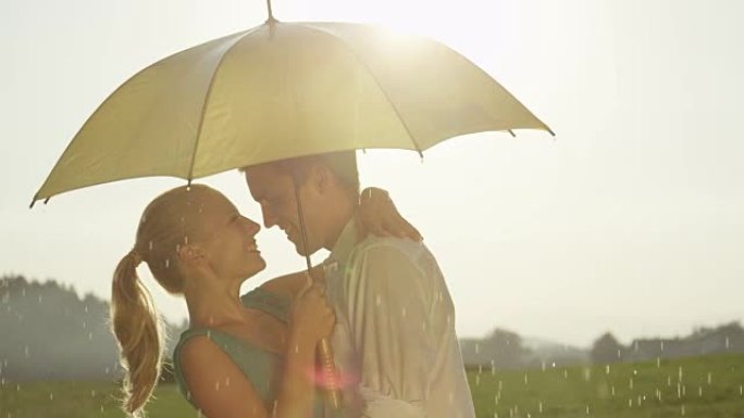 慢动作: 可爱的年轻夫妇在清新的夏雨中微笑和亲吻。