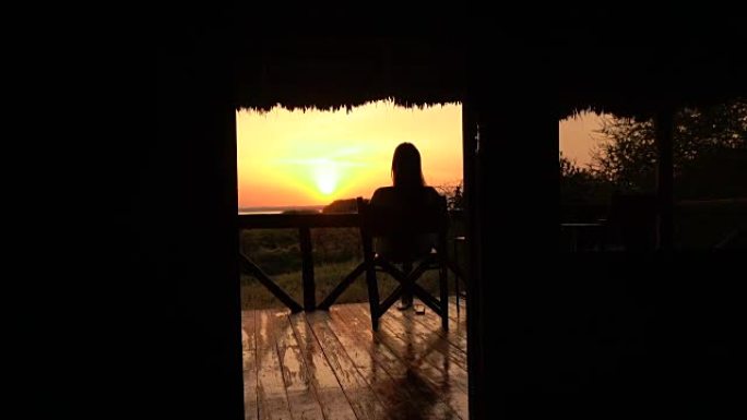 特写: 女孩在阳台上的木椅上放松，看着金色的日出