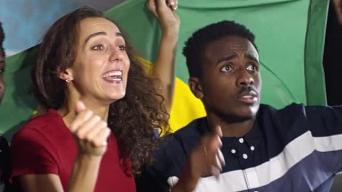 巴西队的球迷在电视上观看足球并举着旗帜