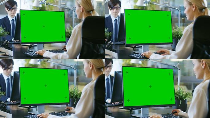 在办公室里，女商人在办公桌前工作，使用带有绿屏模型的个人计算机。同事坐在她对面。现代外观的房间，玻璃