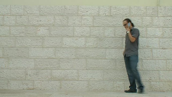 一名男子在白色砖墙附近拿着手机